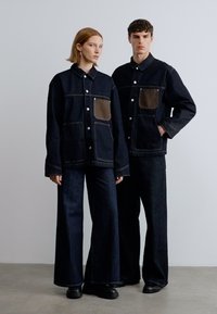 Τζιν μπουφάν και παντελόνι σε σκούρο μπλε, με καφέ τσέπες και ραφές σε αντίθεση. Κούμπωμα με κουμπιά στο μπουφάν, άνετη εφαρμογή και σχεδιασμός με φαρδιά μπατζάκια.