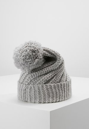 Bonnet d'hiver gris tricoté avec un gros pompon sur le dessus, présenté sur un piédestal blanc sur un fond uni.