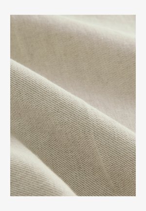 Tessuto beige intrecciato con un motivo a spina di pesce, caratterizzato da una texture morbida e una leggera lucentezza, piegato in dolci ondulazioni.