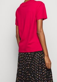 Lys pink bomulds T-shirt med korte ærmer og rund hals, parret med en sort nederdel med et blomsterprint i flere farver.