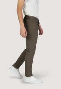 Pantaloni khaki slim-fit con una texture liscia, cinque tasche e chiusura con zip, abbinati a scarpe da ginnastica bianche per un contrasto.