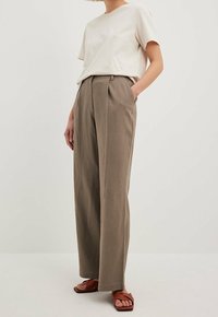 Beżowa bawełniana koszulka zestawiona z wysokimi, luźnymi spodniami w odcieniu taupe z przodowymi zakładkami i bocznymi kieszeniami. Uzupełniona brązowymi sandałami.