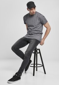 Pilkas marškinėliai su slim-fit juodomis džinsomis, turinčiomis tekstūrą. Juoda kepurė ir juodi sportbačiai su baltais padais užbaigia aprangą.