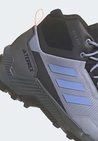 Scarpa da trekking grigio scuro e grigio chiaro con accenti blu, materiale rinforzato, mesh testurizzato, tallone rinforzato e suola Traxion.