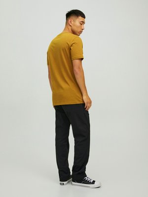 Mustard yellow t-shirt, crew neckline, short sleeves; paired with black pants, relaxed fit; worn with black sneakers featuring white accents.