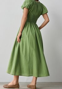 Vihreä puuvillainen midi-mekko, jossa on puffihihat ja rypytetty vyötärö, sekä.TEXTUROITUNEN kuvio. Yhdistettynä kudottuihin vaaleanruskeisiin sandaaleihin.