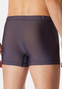 Navy blue swim trunks with thin orange stripes, elastic waistband, and a fitted design. Smooth texture with a small leg opening detail.