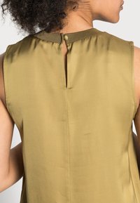 Top sin mangas de color verde oliva con un diseño de espalda con ojal, textura suave, tejido blando y un pequeño cierre de botón en el cuello.