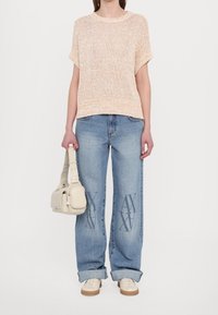 Pull court en maille pêche clair, jeans bleu oversize avec imprimé du logo "AX" et sac à main beige. Des baskets blanches complètent la tenue.