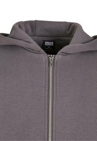 Szürke zipzáras kapucnis pulóver, puha textúrával, ezüst szíjjal és kapucnival. A címke szerint "URBAN CLASSICS", M-es méret, Kínában készült.