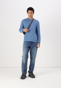 Ljusblå stickad tröja med ribbad nederkant, som är matchad med blå jeans och svarta sneakers. Modellen bär en mörk axelväska.