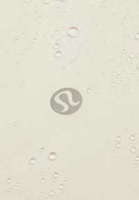 Beige fabric surface with water droplets; features a textured, metallic logo in the center.