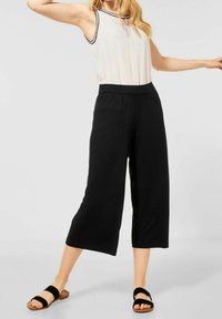 Svarta vida byxor med skräddarsydd passform, som har en mjuk textur och resårmidja. I kombination med en ljus ärmlös topp och svarta sandaler.