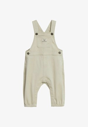 Beige Kinderlatzhose mit verstellbaren Schultergurten, vorderer Brusttasche mit kleinem "minories"-Logo-Patch und Druckknöpfen.