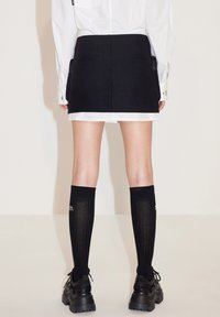 Zwarte minirok met een op maat gemaakt ontwerp, gecombineerd met knie-hoge zwarte sokken en chunky zwarte schoenen. Witte blouse zichtbaar erboven.