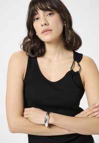 Sort ribbet top med en knude detalje på den ene skulder og en sølv hardware accent. Båret med et elegant metallic armbånd.