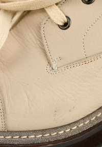 Gros plan sur une chaussure en cuir beige avec des lacets crème, des œillets métalliques, des coutures détaillées et un bord de semelle texturé.