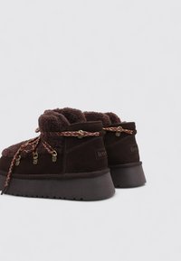 Botines de ante marrón con forro de felpa, con herrajes de tono dorado y cordones multicolores. Suelas gruesas y texturizadas.