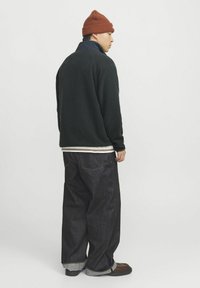 Mørkegrøn fleece-pullover med en marineblå krave, parret med løse mørke jeans med opfoldede ben og brune sko. Brun beanie på hovedet.
