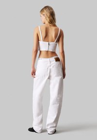 Top corto bianco con zip sul retro, abbinato a jeans bianchi a gamba larga. Tessuto liscio con spalline regolabili e un design semplice e pulito.