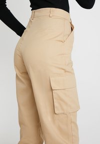 Beiga cargobyxor med hög midja, med en sidoficka, tillverkade av en mjuk bomullsblandning med en jämn textur.