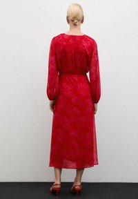 Rode midi-jurk met bloemenpatroon, lange doorzichtige mouwen, een cinched taille en een losvallende pasvorm, gecombineerd met rode hoge hakken. Achteraanzicht weergegeven.