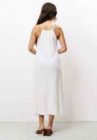 Weißes, ärmelloses Maxikleid aus strukturiertem Stoff, mit gerafftem Rücken und Bindeband. Kombiniert mit braunen Blockabsatzsandalen.