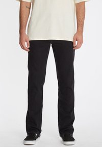 Zwarte denim jeans met een rechte pijp, met een klassiek ontwerp, subtiele textuur en gecombineerd met zwarte sneakers en een lichtgekleurde t-shirt.