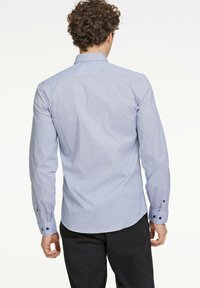 Camicia azzurra chiara con piccoli motivi geometrici blu navy, maniche lunghe, polsini a bottone e colletto classico, realizzata in tessuto morbido.