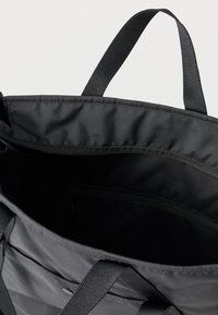 Fekete szövet bevásárlótáska masszív pántokkal, tágas belső résszel és cipzáras zsebbel. A belső része sima, matt textúrájú.