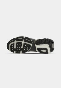 Semelle en caoutchouc noire et blanche d'une chaussure de sport montrant des motifs de la bande de roulement pour la traction et l'adhérence sur fond blanc.