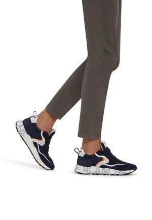 Des chaussures de sport bleu marine et blanches présentent un dessus texturé, des accents orange contrastants et une semelle épaisse avec un détail de marque.