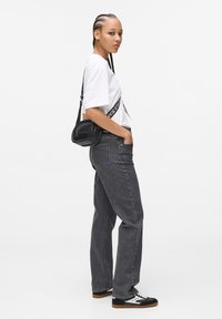 Jeans in denim grigio con una vestibilità comoda, abbinati a una maglietta bianca con una grafica nera. Borsa a tracolla nera e sneakers nere con dettagli bianchi.