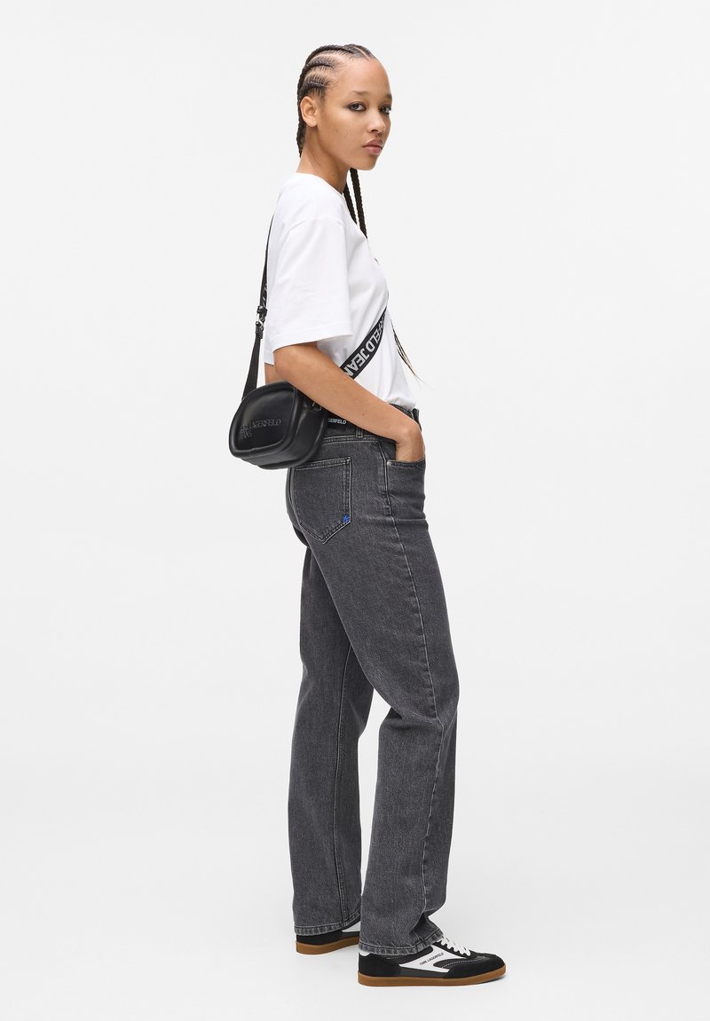 Jeans in denim grigio con una vestibilità comoda, abbinati a una maglietta bianca con una grafica nera. Borsa a tracolla nera e sneakers nere con dettagli bianchi.