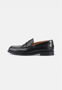 Svarta läderloafers med rund tå, präglade detaljer på ovansidan och en slät yta; har en låg klack och en flexibel sula.