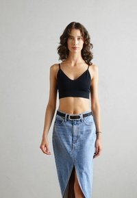 Fekete bordázott crop top, amelyet egy magas derekú, világoskék farmer szoknyával viselnek, elöl résnyílással és fekete övvel, ezüstcsattal.