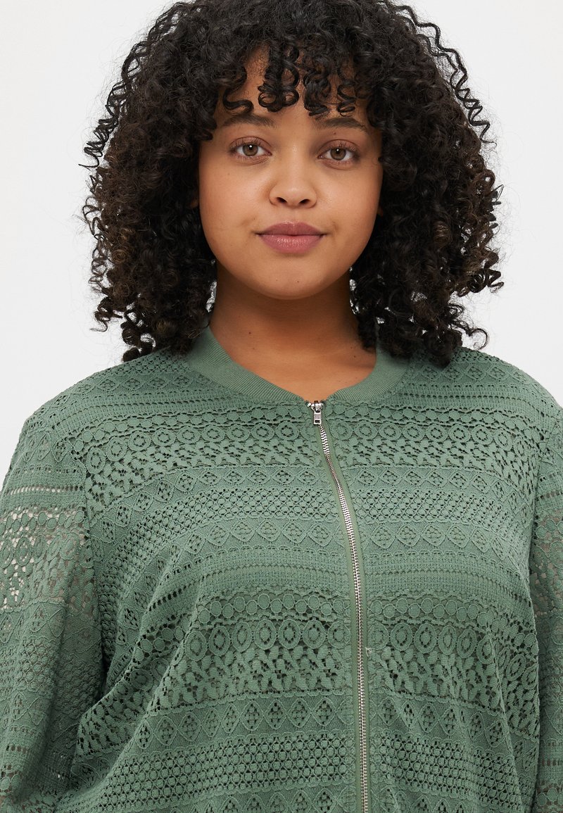 Jasnozielona bomberka z koronką z zapięciem na zamek, teksturowanymi wzorami, ściągaczem w kołnierzu i mankietach, oraz luźnym fasonem z detalicznym wykończeniem szwów.