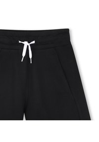 Pantalons de survêtement noirs avec une texture lisse, dotés d'une taille à cordon blanc, de deux poches latérales et d'une étiquette de marque discrète sur la taille.