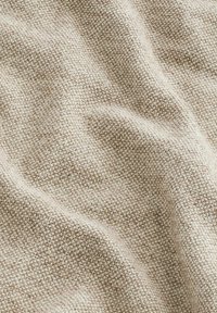Beige tekstureret stof med et vævet mønster, der har en blød, let hævet overflade og subtile farvevariationer gennem hele stoffet.