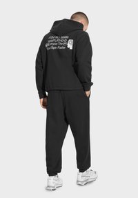 Czarna bluza z kapturem z graficznym napisem z tyłu, luźny krój, wykonana z mieszanki bawełny, w zestawie z dopasowanymi spodniami i białymi trampkami.