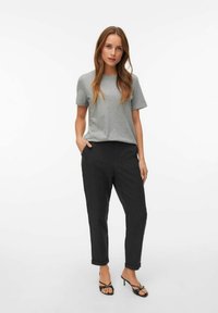 T-shirt grigio a maniche corte abbinato a pantaloni scuri grigi a gamba affusolata. I pantaloni hanno un risvolto e una texture di tessuto liscia. Sandali neri con cinturini.