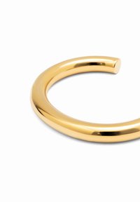 Pulsera de metal dorado con un diseño suave y redondeado y acabado brillante. Presenta una forma circular continua sin ningún tipo de cierre.