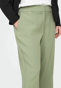 Heledad rohelised püksid, millel on mugav lõige, sile tekstuur, küljetaskud ja lame vöökoht. Rikkastatud peente õmbluste detailidega.