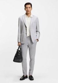 Blazer grigio chiaro, polo color crema, pantaloni chiari coordinati e borsa in pelle nera. Tessuto liscio, taglio sartoriale, design con doppi bottoni, dettagli minimalisti.