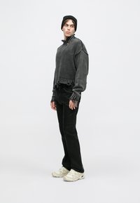 Γκρι κοντό πουλόβερ με βολάν στη λαιμόκοψη, μαύρο παντελόνι και λευκά αθλητικά παπούτσια. Το σύνολο έχει υφή πλεκτού υλικού και διακριτικές φθορές.