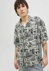 Camisa de manga corta con cuello en una tela color crema que presenta un patrón abstracto negro con motivos inspirados en la naturaleza y formas geométricas.