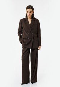 Bruine dubbelknopen blazer met een notch kraag, twee voorzakken en bijpassende brede broek, gemaakt van textuurstof.