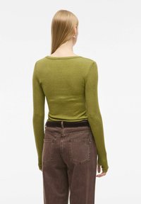 Dolgimi rokavi, olivno zelena majica z okroglo ovratnikom, v kombinaciji z rjavimi hlačami z visokim pasom, ki imajo zadnje žepe in detajle šivanja.