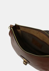Borsa in pelle marrone con zip dorata, mostra un morbido rivestimento interno, tasca interna e un dettaglio di hardware circolare sulla parte anteriore.