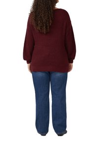 Diep rode gebreide trui met verlaagde schouders en lange mouwen, gecombineerd met blauwe jeans met een relaxte pasvorm. Ribgebreide zoom en manchetten, textuurstof.